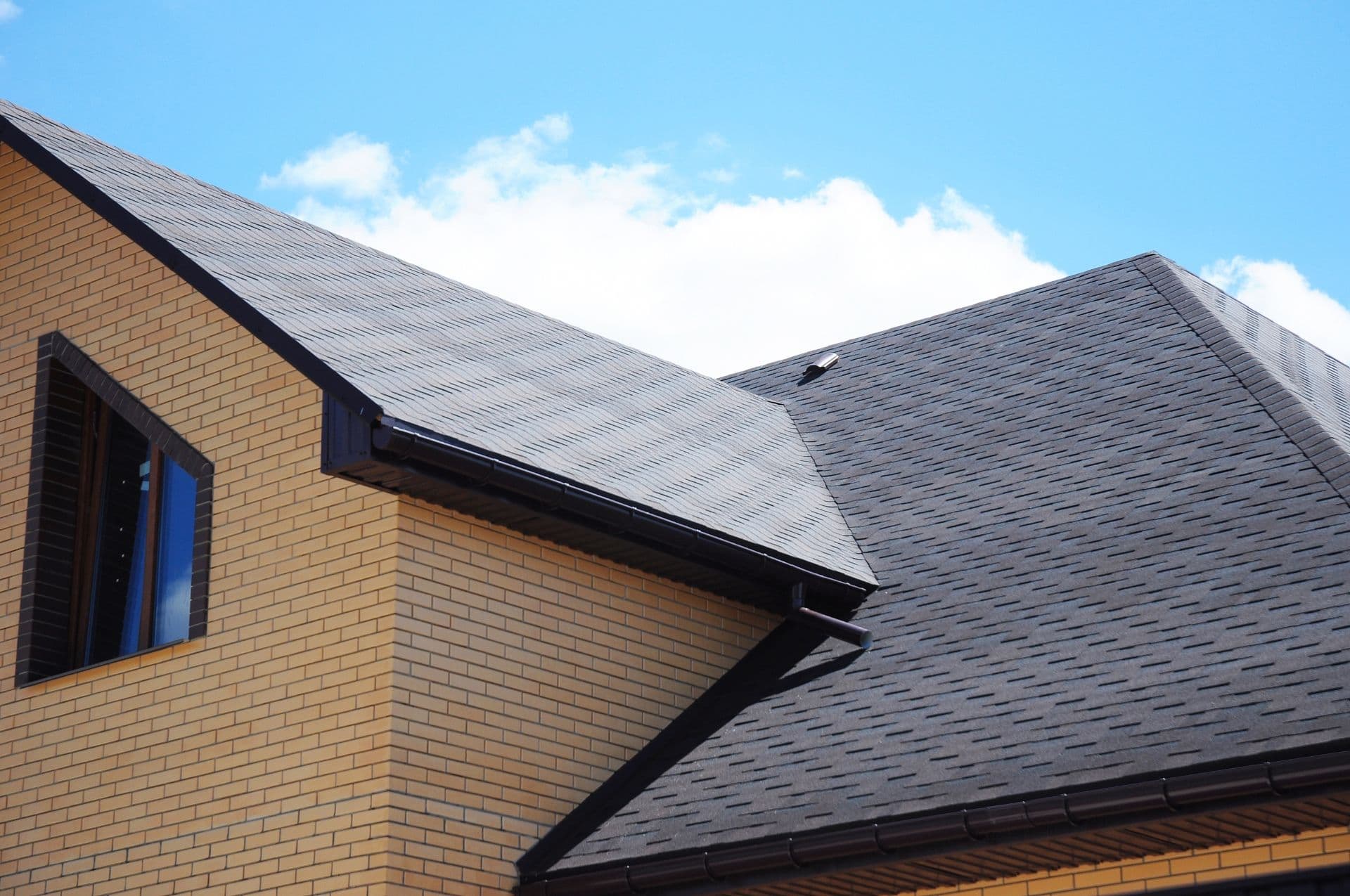 Brick house with a steep, dark shingle roof under a clear blue sky. A single window is visible, creating a clean and modern appearance.