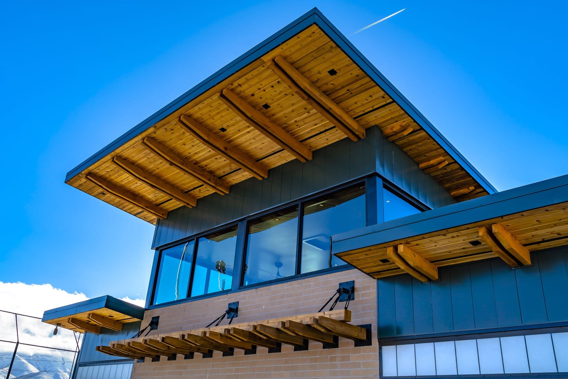 Modern building with a sloped wooden roof and large glass windows against a clear blue sky. The structure conveys a sleek and contemporary design.