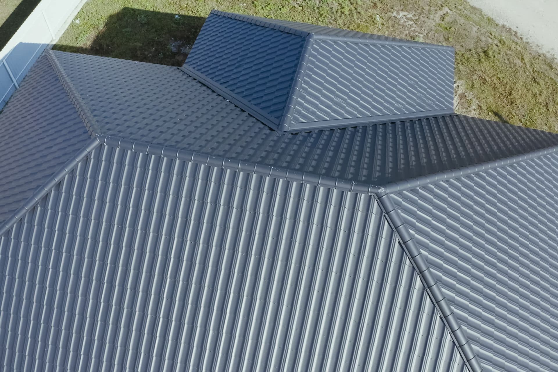 Aerial view of a modern, gray metal roof with clean lines and textured panels. The structure is symmetrical and situated against a grassy area.